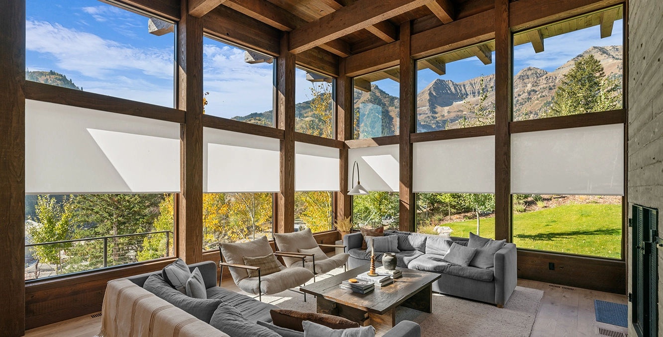 Beige roller shades in tall windows with wooden beam ceilings. Outlooking a mountain scenery