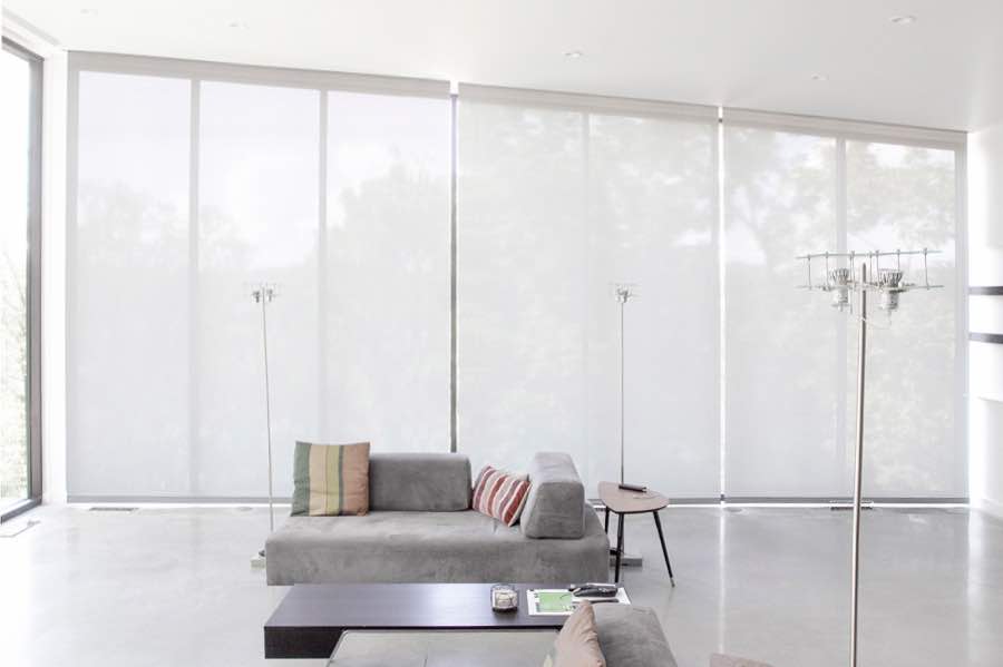 Motorized window shades make controlling natural light effortless in your Southern California great room. White motorized shades on a wall of tall great room windows