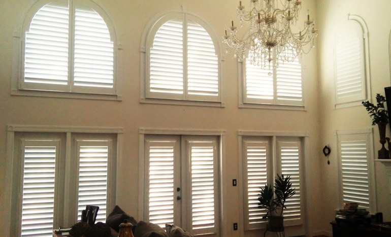 Television room in two-story Southern California house with plantation shutters on high windows.