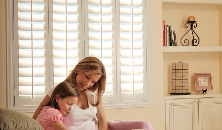 Easy to clean faux wood shutters are great cord-free options for children. Mom and daughter in front of window
