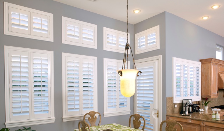 Interior Shutters can fix both sun glare and heat loss problems. White plantation shutters in dining room